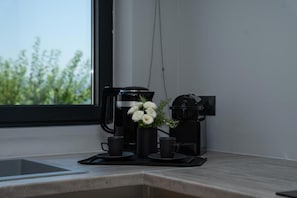 A kitchen counter with a coffee maker, a small vase with white flowers, and two black cups. - Cavalier Suites Nikiana Lefkada AV Properties (Lefkada)
