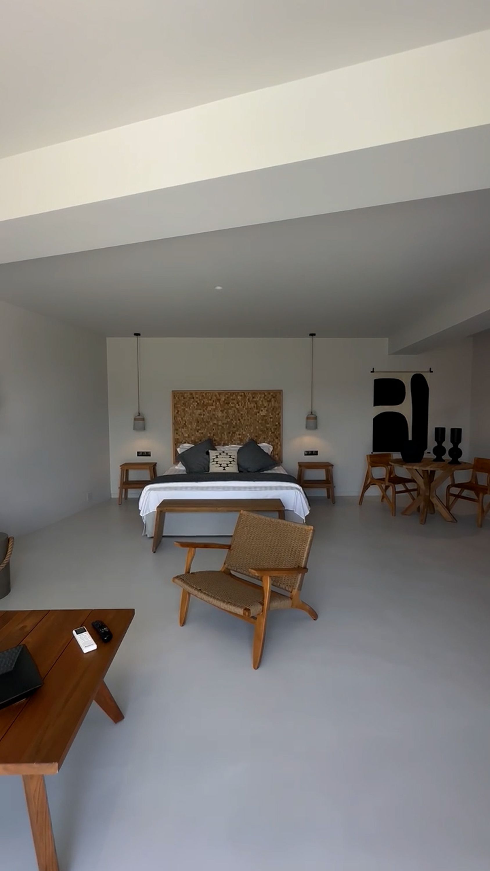 Et moderne soveværelse med en stor seng, en træstol, et lille bord og et spiseområde med stole.