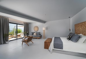 A modern bedroom with a large bed, a wooden bench, a sofa, and a chair. There is a large window with curtains, a lamp, and a wall-mounted clock. - Cavalier Suites Nikiana Lefkada AV Properties (Lefkada)