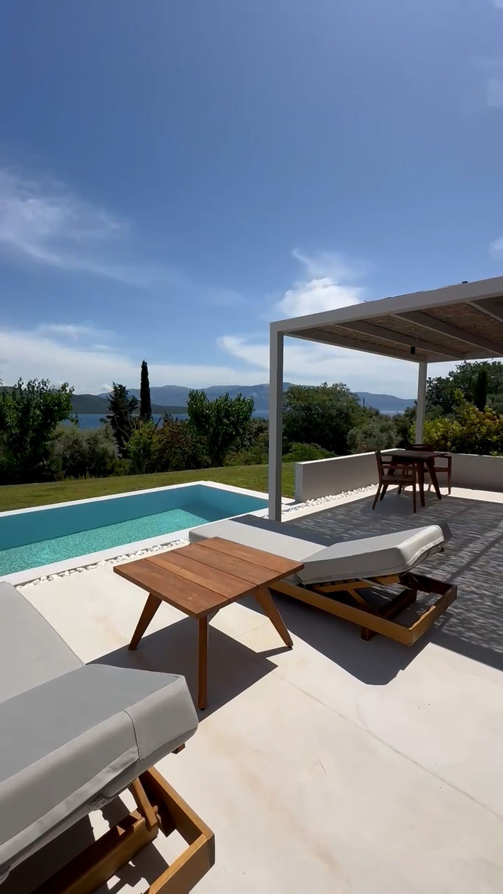 A poolside area with a view of the sea, a pergola, and outdoor furniture.