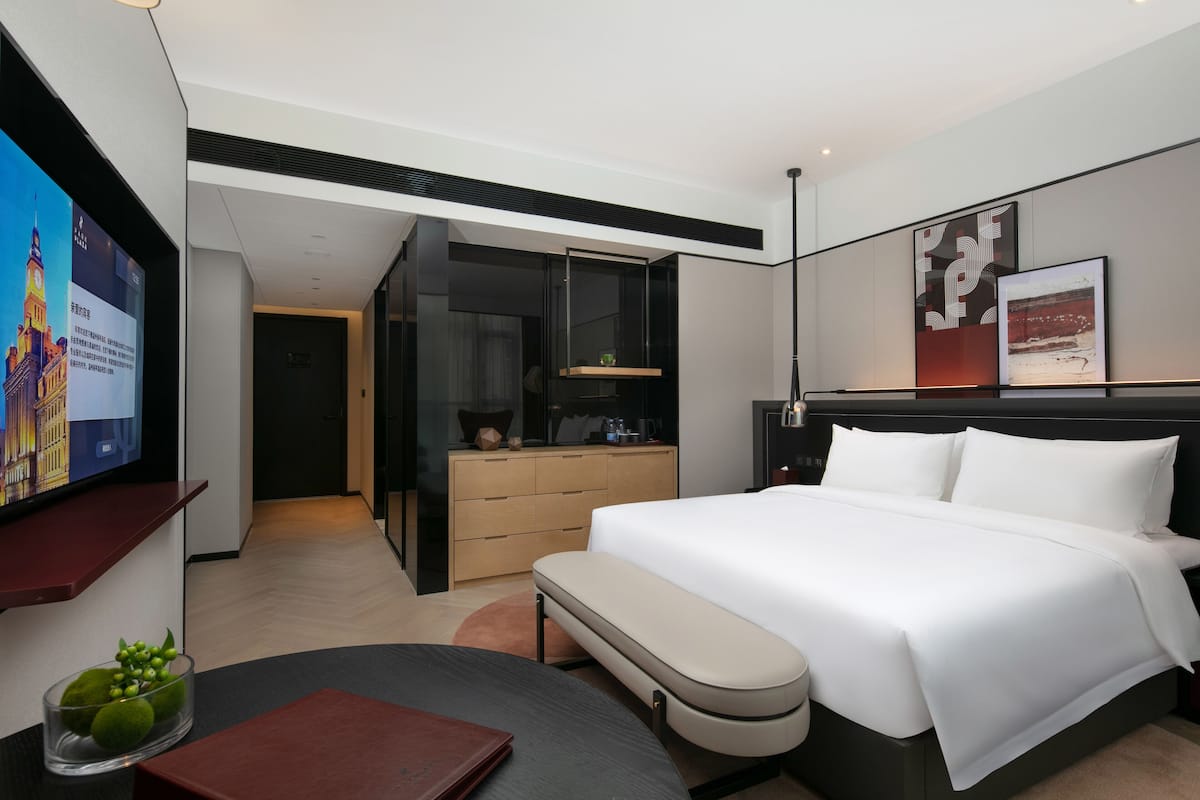 Ein modernes Hotelzimmer mit einem großen Bett, einem Schreibtisch, einem Fernseher und einem durch eine offene Tür einsehbaren Badezimmer.