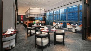 A modern dining area with round tables, white chairs, and a bar in the background. - Park Plaza Wenzhou (Wenzhou)