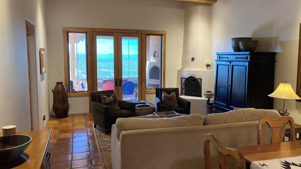 Una sala de estar con sofá, sillas, una mesa de madera, un aparador y vistas a través de amplios ventanales.