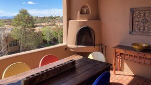 Un balcón con una mesa de madera, sillas, un horno de pizza y vistas a un barrio residencial.