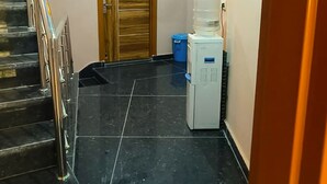 Un pasillo con una escalera, una puerta de madera, un dispensador de agua y un electrodoméstico blanco pequeño.