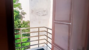 Un balcón estrecho con barandilla de metal, suelo de hormigón y vistas a zonas verdes.