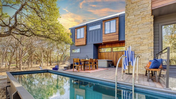 Una casa moderna con piscina, mobiliario exterior y un muro de piedra.