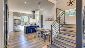 Una cocina amplia con una isla central, un comedor con sillas y una escalera que sube a un nivel superior.