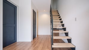 A modern staircase with wooden steps and black metal railings, leading to a landing with a white door and a light fixture. - VillaSanctuary＆SaunaOgimi (Ogimi)