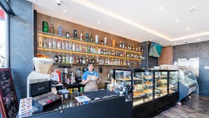 A modern bar area with a variety of liquor bottles on shelves, a coffee machine, and a display case with pastries.