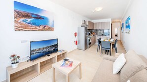 Un appartement moderne comprenant un salon, un coin repas et une cuisine. On y trouve une grande télévision, un canapé et une table à manger avec des chaises.