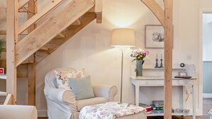 Une pièce chaleureuse avec un escalier en bois, un fauteuil confortable, un bureau avec une lampe et un vase rempli de fleurs.