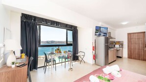 A hotel room with a balcony, a dining area, a kitchen, and a bed with towels. - Islet Promenade Seaview Studio (Bugibba)