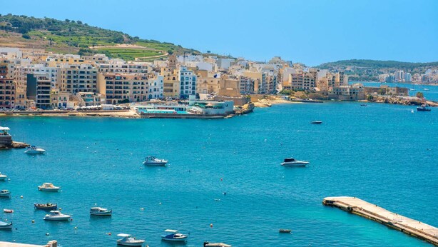 A coastal cityscape with buildings along the waterfront, boats in the water, and a clear blue sky. - Islet Promenade Seaview Studio (Bugibba)