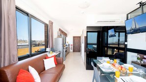 A modern apartment with a living area, kitchenette, dining space, and a balcony with a city view. - Islet Promenade Seafront Penthouse with Hot Tub (Bugibba)