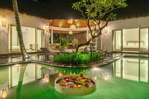 A pool area with a dining setup, lounge chairs, and a thatched-roof structure.