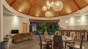 Um espaço interno amplo com teto alto, uma mesa de jantar redonda com cadeiras, um banco de madeira e um bar.