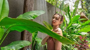 Uma pessoa em um ambiente natural, com um chuveiro, cercada por vegetação exuberante.