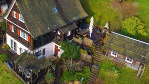 A two-story house with a sloped roof, a small garden, and a wooden deck. - Waldhaus: Sauna Jacuzzi Kamin 16 Pax (Alpirsbach)