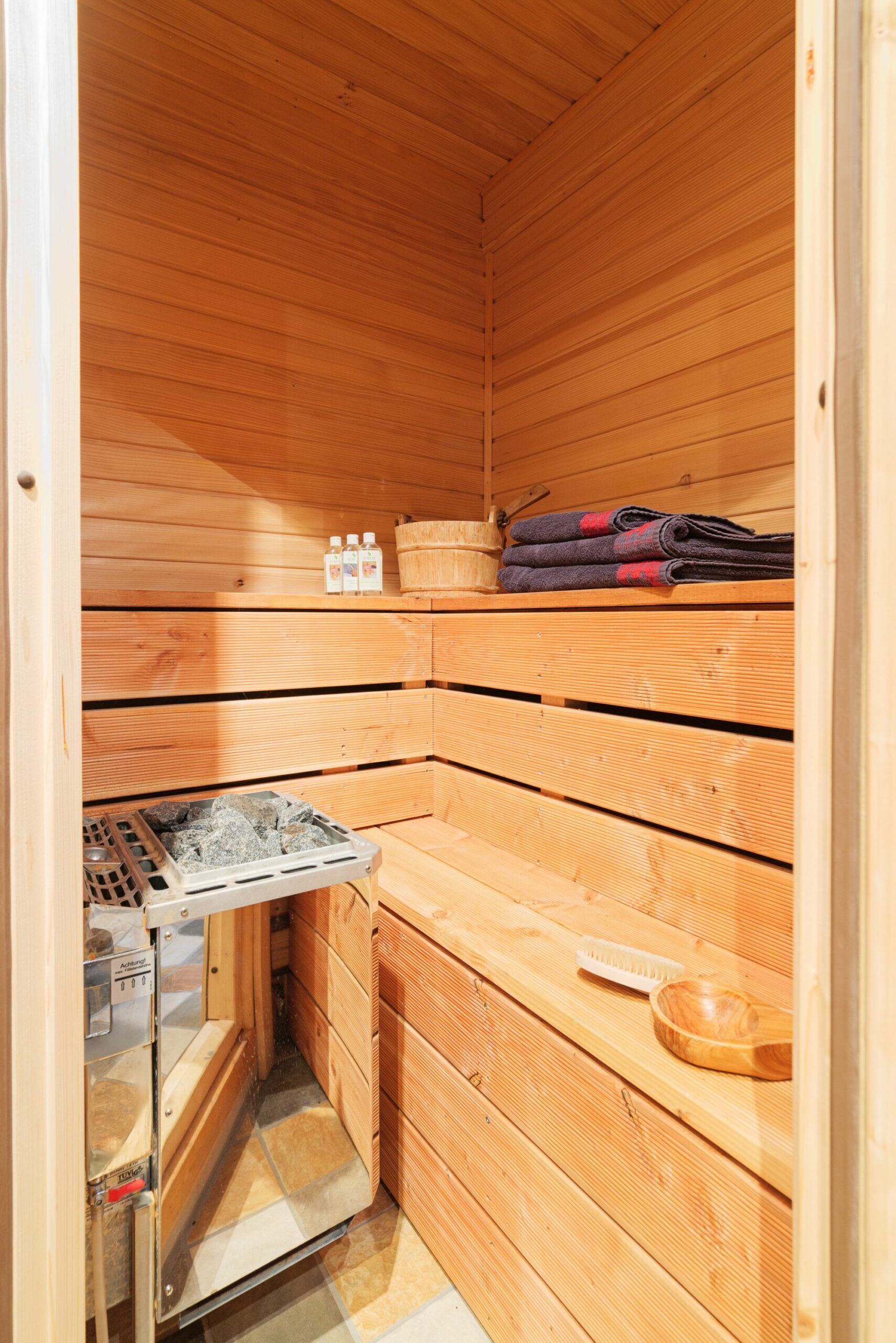 Una sauna con pareti in legno, una panca, uno scaldasalviette, asciugamani e bottiglie.