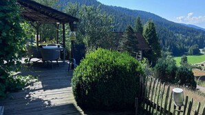 Une terrasse en bois avec des meubles d’extérieur, une pergola et une vue sur une chaîne de montagnes boisée.
