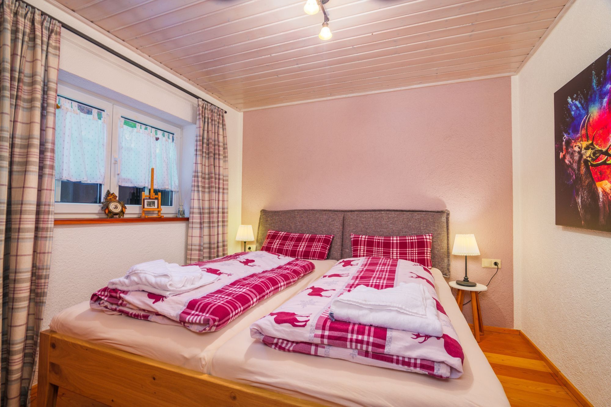Een tweepersoonsbed met hoofdeinde, twee nachtkastjes met lampen, een raam met gordijnen en een schilderij aan de muur.