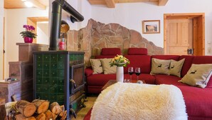 Un salon chaleureux avec un mur en pierre, une cheminée, un canapé rouge et un tapis blanc moelleux.