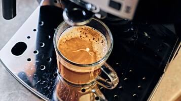 Een glazen kop koffie op een metalen dienblad, met een koffieapparaat op de achtergrond.