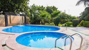 Une piscine divisée en deux zones distinctes, entourée d’une terrasse carrelée et d’une végétation luxuriante.