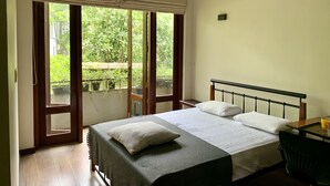 A bedroom with a bed, a ceiling fan, a window with a view of greenery, and a table with a chair. - Cozy luxury room with beautiful views (Battaramulla)