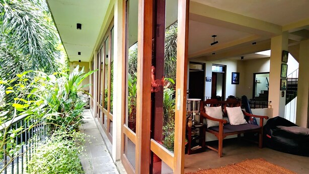 A covered outdoor area with a concrete floor, wooden-framed glass doors, and a seating area with a sofa and cushions. - Cozy luxury room with beautiful views (Battaramulla)