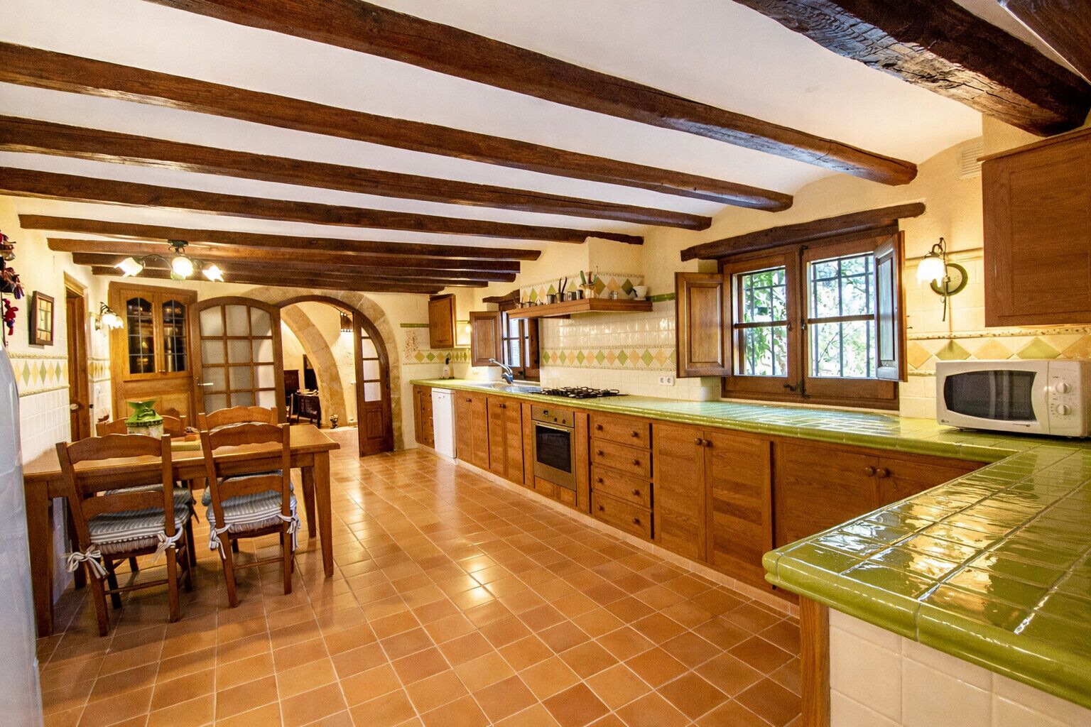 Een keuken met houten kastjes, een groen aanrecht, een magnetron en een eethoek met stoelen en een tafel.