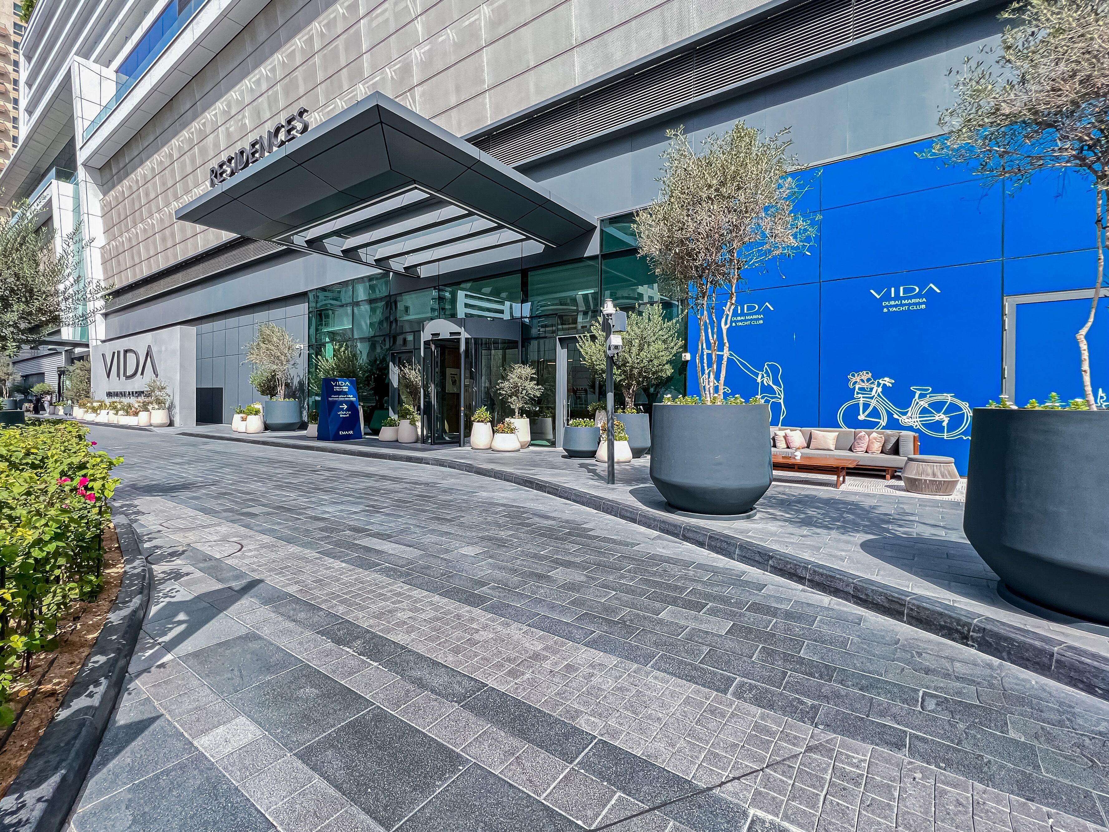 A modern building with a glass facade, a blue wall with a bicycle graphic, and a sign for 'VIDA'.