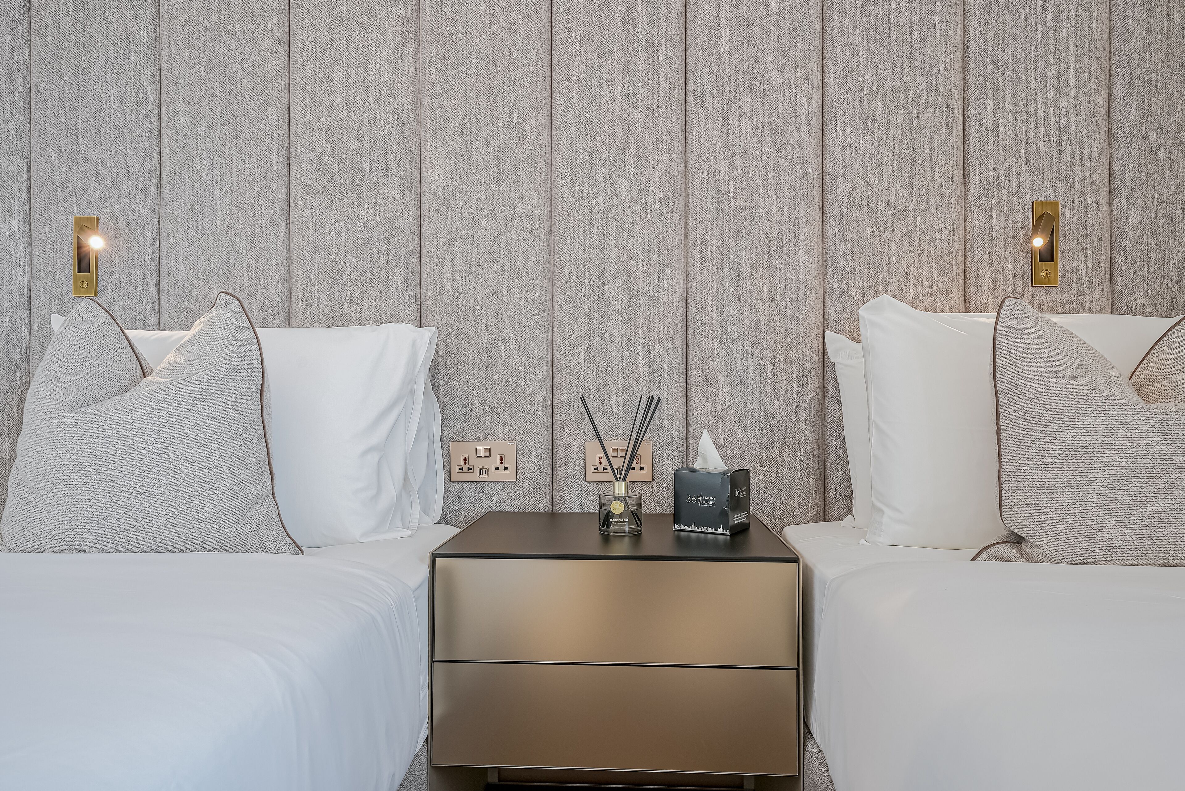 A hotel room with two beds, a nightstand, and a wall-mounted light fixture.