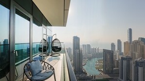 A balcony with a glass railing, two chairs, and a view of a cityscape with tall buildings and a river. - Modern 2BR HighFloor Haven - Vida Marina (Dubai)