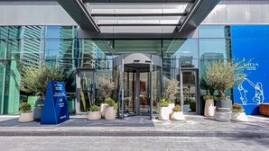 A modern building entrance with glass doors, potted plants, and a blue sign indicating a customer home office. - Modern 2BR HighFloor Haven - Vida Marina (Dubai)