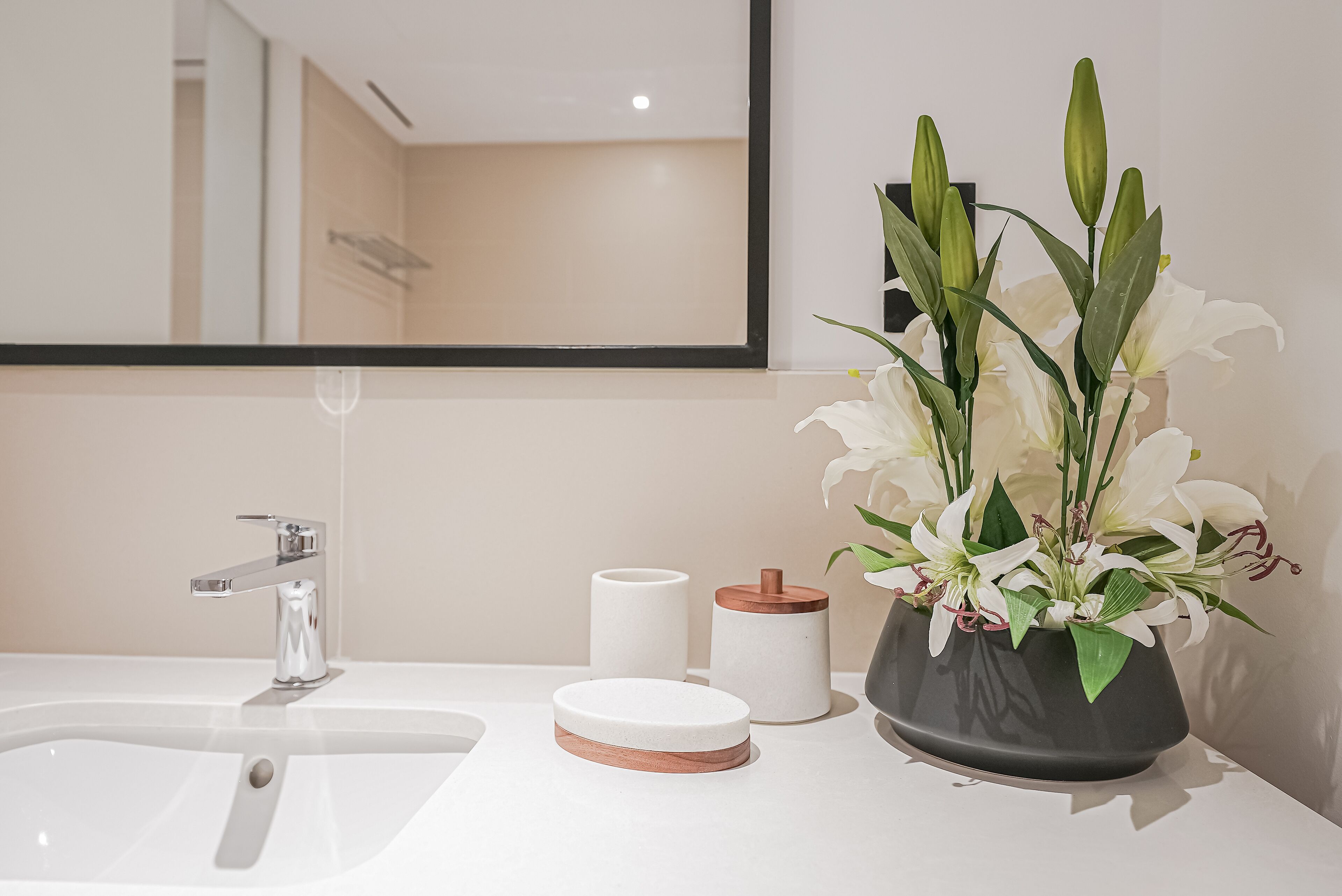 A bathroom with a white sink, a mirror, a towel rack, and a vase with white flowers.