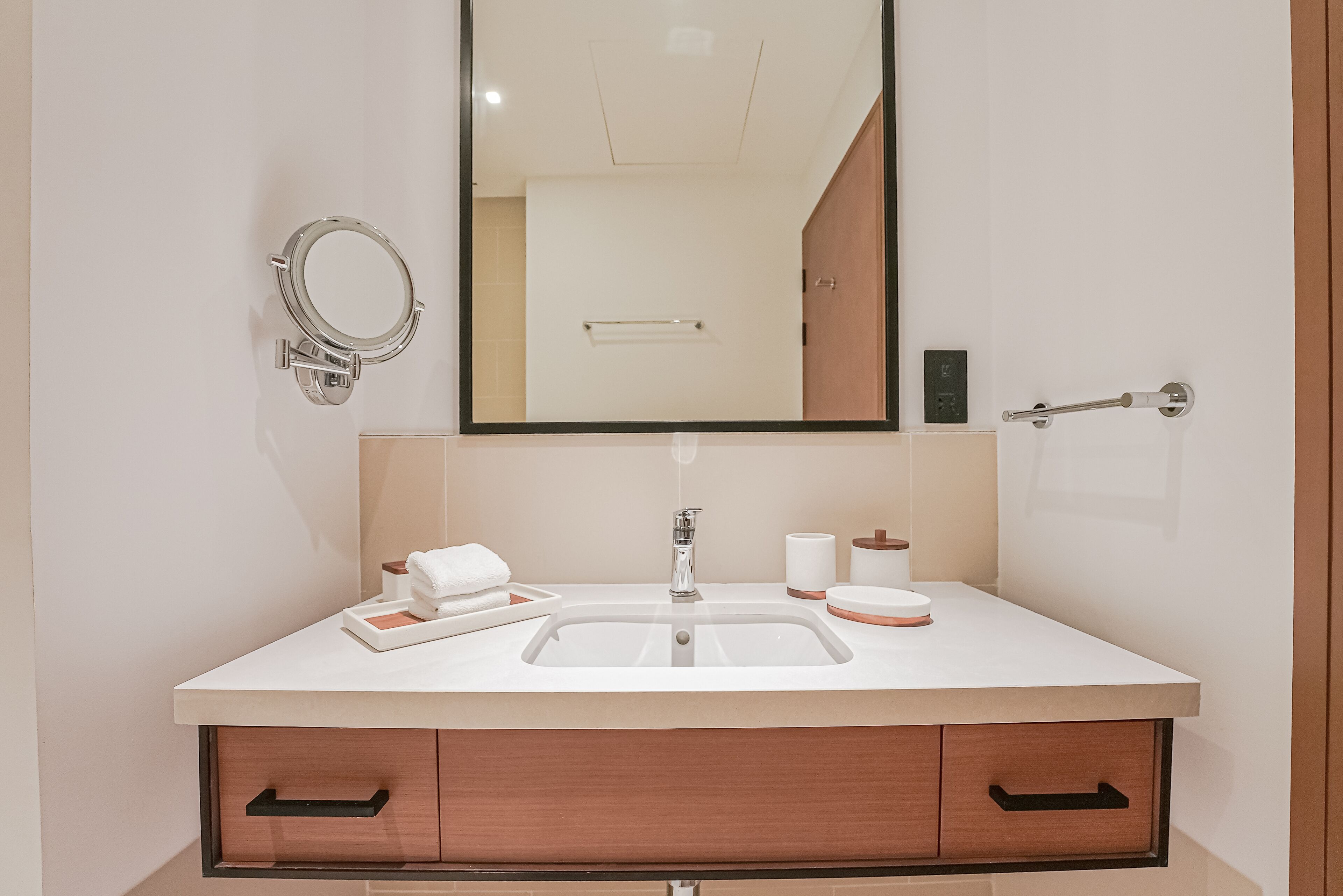 A modern bathroom with a white sink, a mirror, a towel, and a toilet paper holder.
