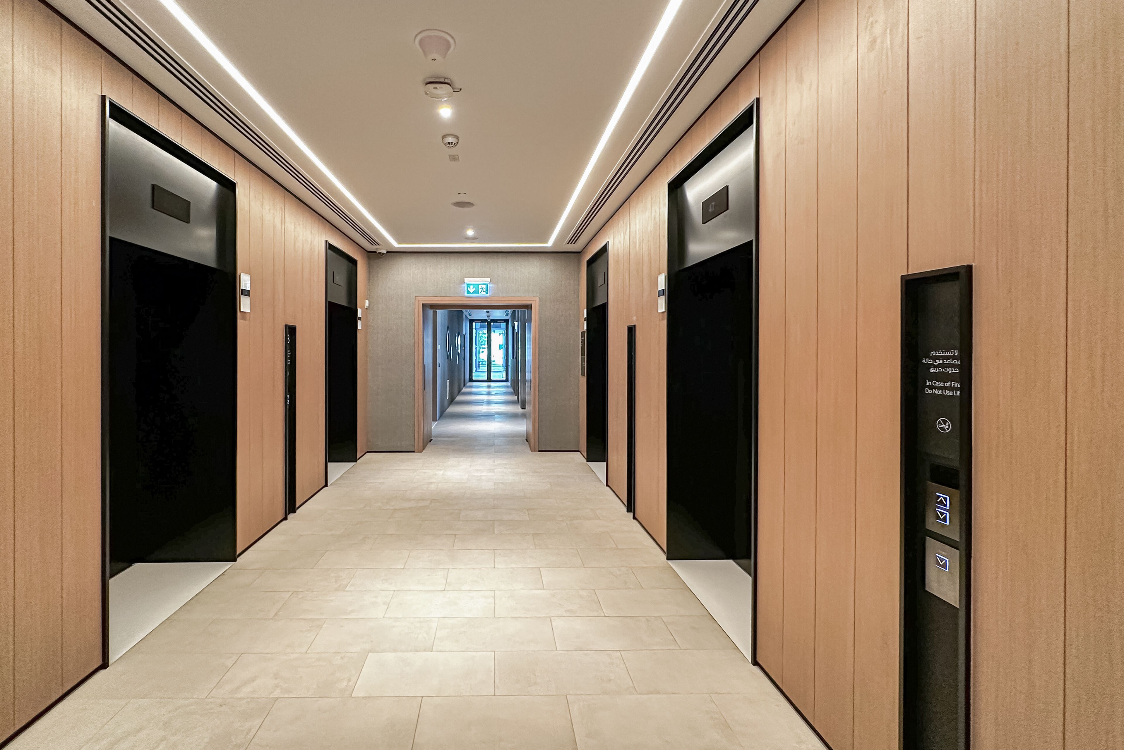 A modern hotel corridor with wooden paneling, a tiled floor, and a straight path leading to an exit.