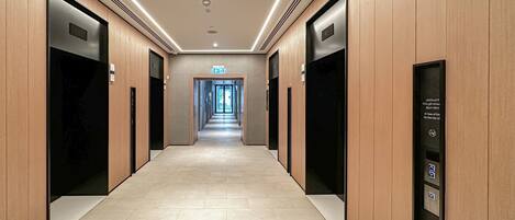 A modern hotel corridor with wooden paneling, a tiled floor, and a straight path leading to an exit.