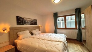 Une chambre à coucher avec un lit, des lampes de chevet, une fenêtre avec des rideaux, un radiateur et un tableau accroché au mur.