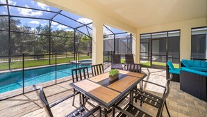 Eine Terrasse im Freien mit Pool, einem Holztisch und Gartenmöbeln.