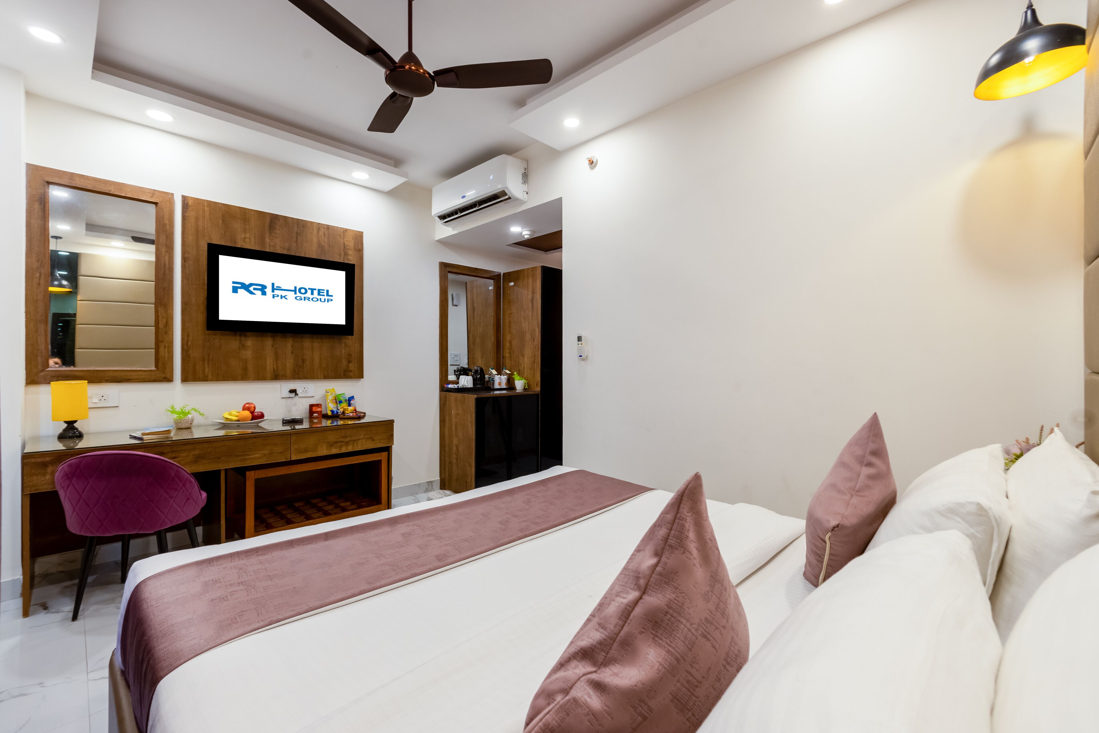 Habitación de hotel con cama, escritorio, silla, televisor y ventilador de techo.