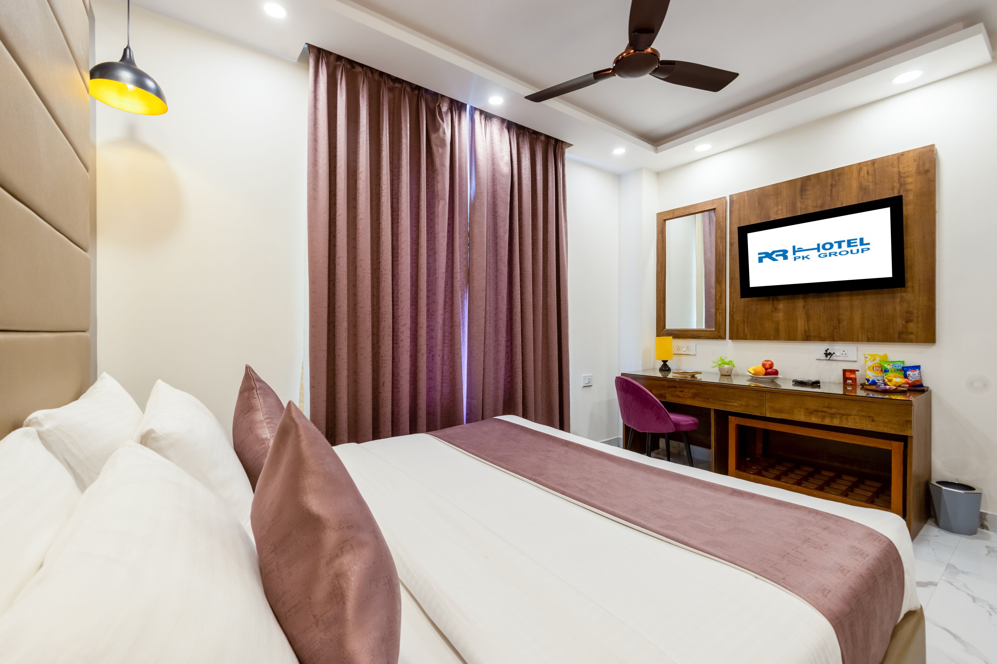 Habitación de hotel con cama, escritorio, silla, ventilador de techo y televisor montado en la pared.