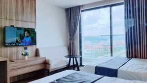 A hotel room with two beds, a TV, a desk, and a view of a cityscape. - Johnny Nguyen - Victor Condotel Phu Yen (Tuy Hoa)