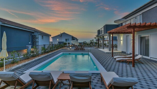 Ein Schwimmbad mit Liegestühlen, einer Pergola und Blick auf den Sonnenuntergang.