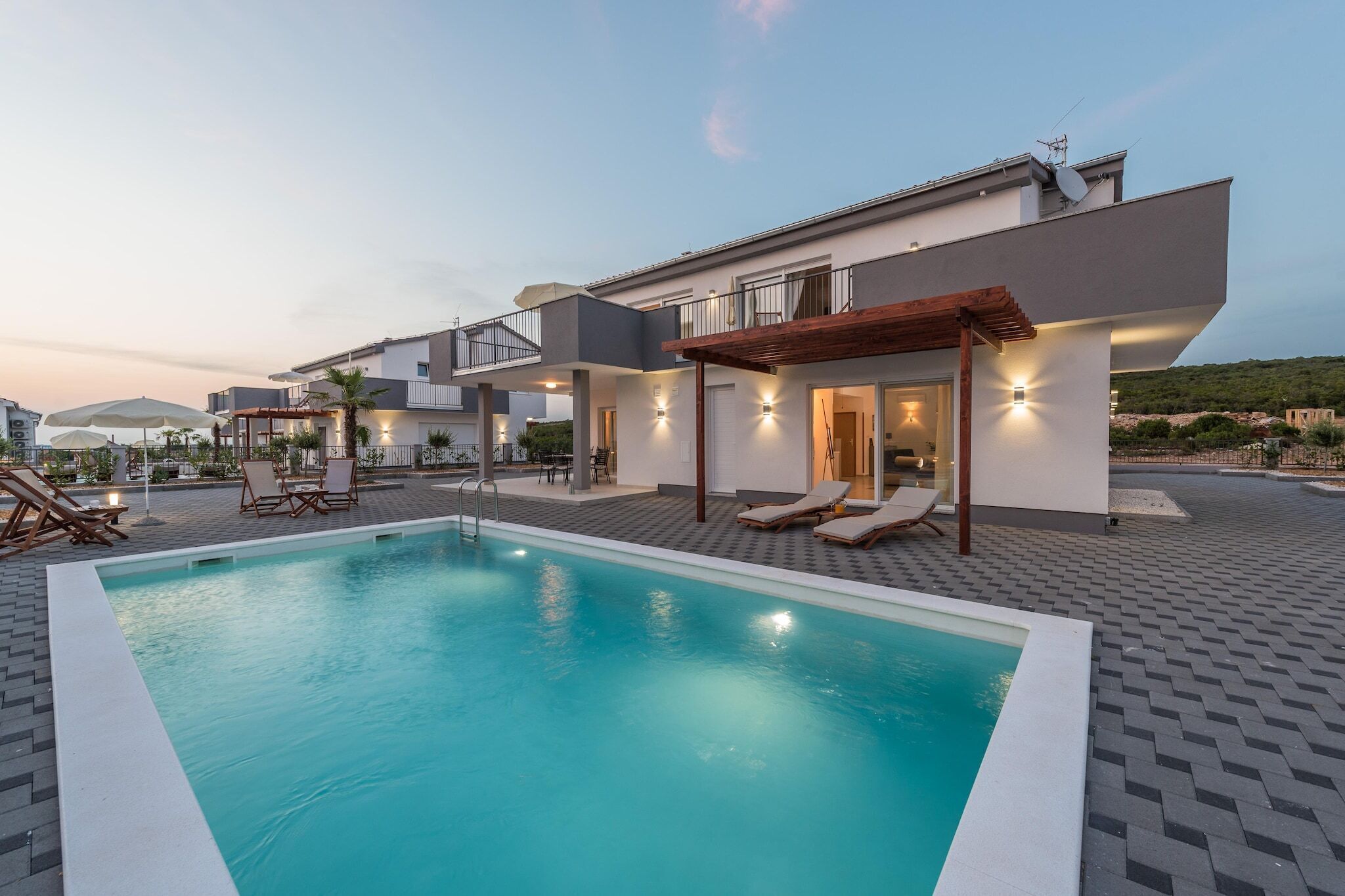 A modern pool area with lounge chairs and a pergola, surrounded by a multi-story building with outdoor lighting.