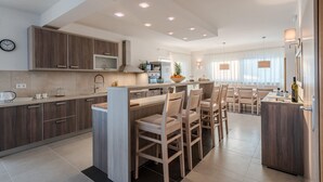 A modern kitchen with wooden cabinets, a central island with bar stools, and a dining area with a table and chairs. - Apartment in Croatia near the Adriatic Coast (Sukosan)