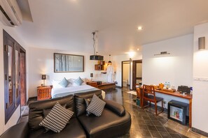 Ein modernes Hotelzimmer mit einem großen Bett, einem Ledersofa, einem Schreibtisch mit Computer und einem kleinen Kühlschrank.