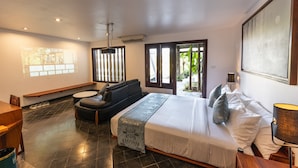 Une chambre d’hôtel moderne, dotée d’un grand lit, d’un canapé, d’un bureau et offrant une vue sur la verdure par les fenêtres.